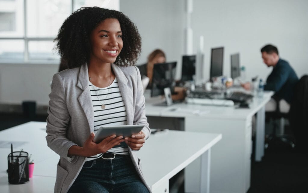 Diverse professional woman holding tablet in modern office environment.