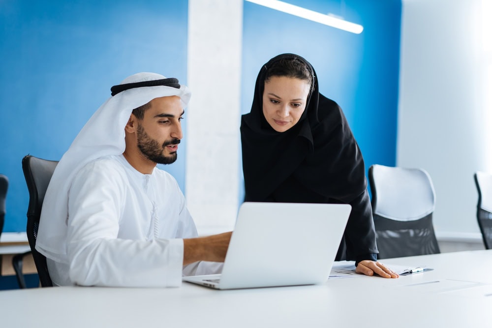 Arab man and woman discussing project on laptop in conference room.