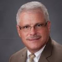 Experienced professional with white hair and glasses in a suit.