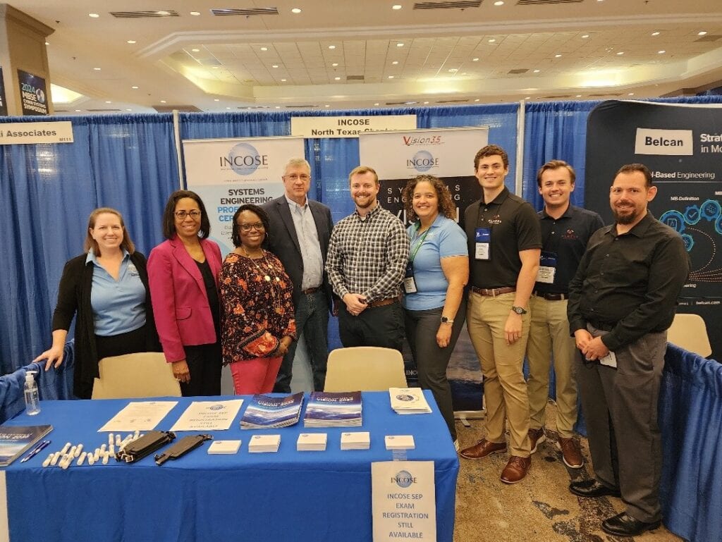 Diverse group of professionals at INCOSE conference booth in a large event hall.