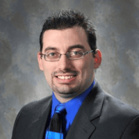 A professional man in a suit smiling against a gray background.