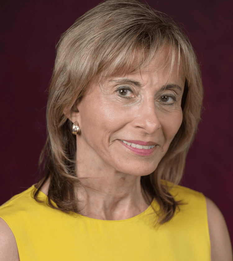 Senior woman in yellow dress smiling, professional headshot, conference or business portrait.