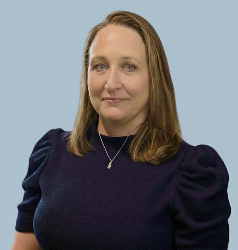 Focused professional woman with red hair wearing a navy blouse, smiling confidently.