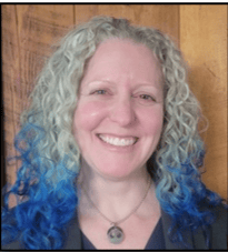 A smiling woman with curly hair and blue ombre tips, wearing a necklace.