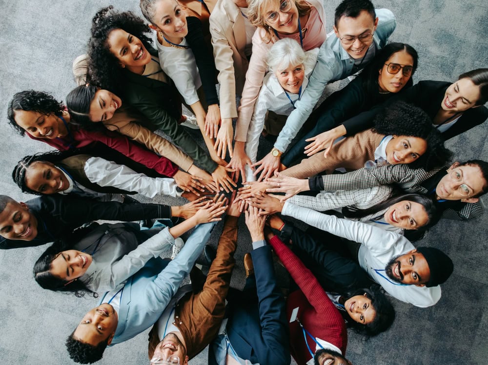Diverse group of professionals putting hands together in unity at an office teamwork event.