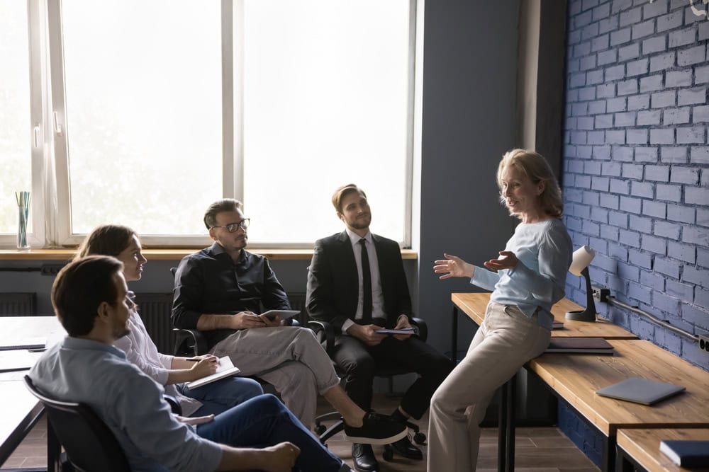 Well-dressed woman giving a presentation to a small team in modern office meeting room.